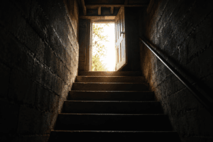 Dark basement stairs leading toward an open door filled with light, symbolizing the decision to seek help for addiction.